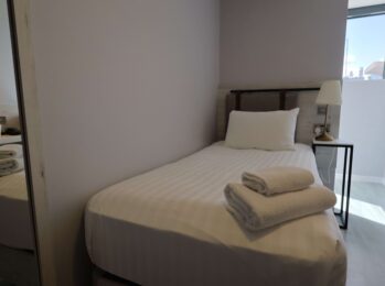 Cosy single hotel room with comfy bed, fresh linens, modern lamp, and natural light from window; ideal for solo travellers.