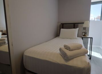 Cosy single hotel room with comfy bed, fresh linens, modern lamp, and natural light from window; ideal for solo travellers.
