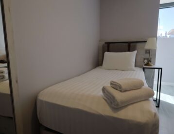 Cosy single hotel room with comfy bed, fresh linens, modern lamp, and natural light from window; ideal for solo travellers.