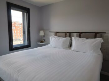 Cosy hotel room with plush double bed, soft pillows, bedside lamps, modern decor, and a city view through the window.