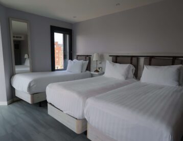 Stylish hotel room with three comfy beds, soft lighting, city views, modern décor, perfect for families or groups.