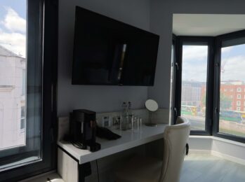 Bright hotel room with large window views, featuring a wall-mounted TV, coffee station, and comfortable workspace.
