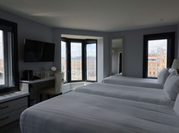 Spacious hotel room with three plush beds, cityscape view, flat-screen TV, and workspace for a comfortable stay.
