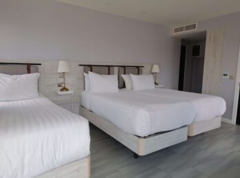Spacious hotel room with king and single beds, crisp white linens, modern decor, and natural light from large window.
