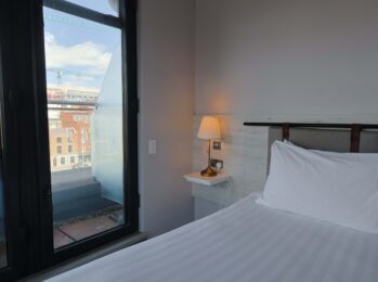 Bright hotel room with city view, cosy bed, soft pillows, bedside lamp; ideal for a serene urban stay near top attractions.