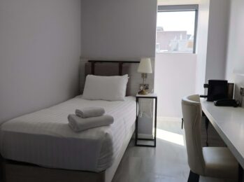 Cosy single room with bed, desk, and city view; features modern decor and ample natural light for a relaxing stay.